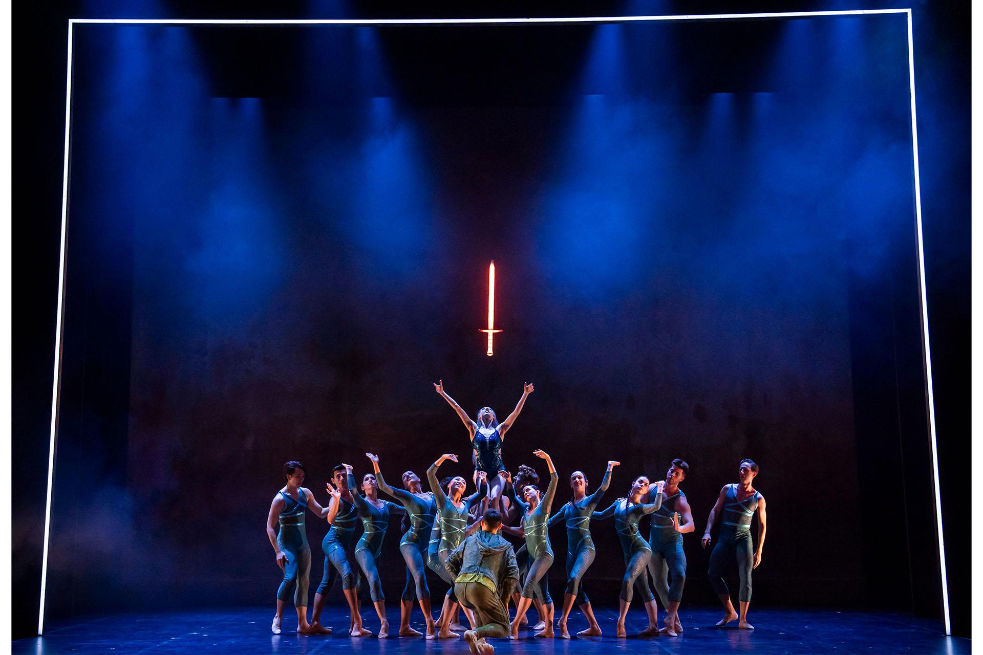 Merlin, 2025, production, Northern Ballet dancers, photo Tristram Kenton The Ladt of the Lake held aloft by dancers representing the waters raises her arms to the glowing sword just above her head