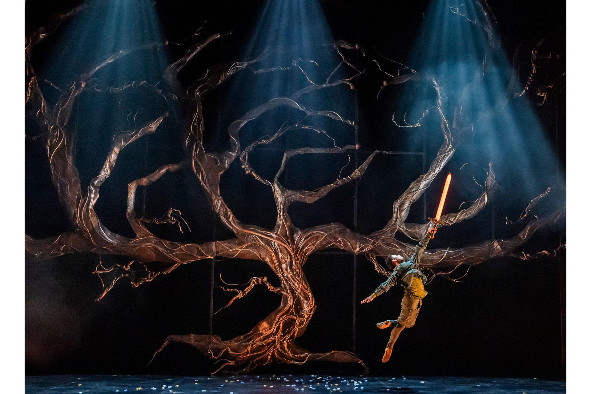 The tree of life, without leaves or magic, Merlin dances in front of it, a glowing sword raised high, inviting the magic into the kingdom