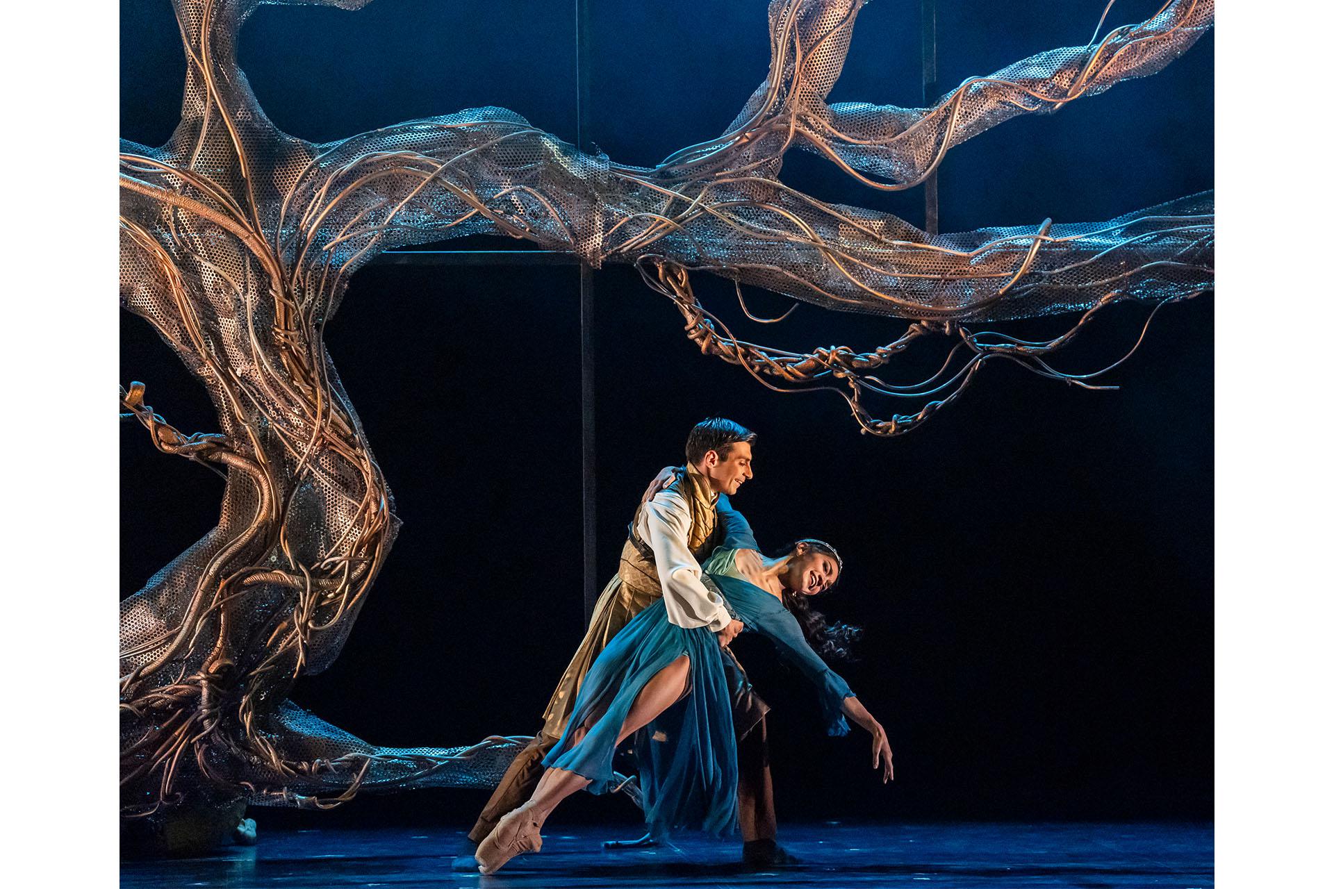 Merlin, 2025, production, dancers Filippo Di Vilio and Rachael Gillespie, photo Tristram Kenton Ygraine and Uther falling in love, dancing under the Tree of Life, he in a golden tunic, her in a blue dress.