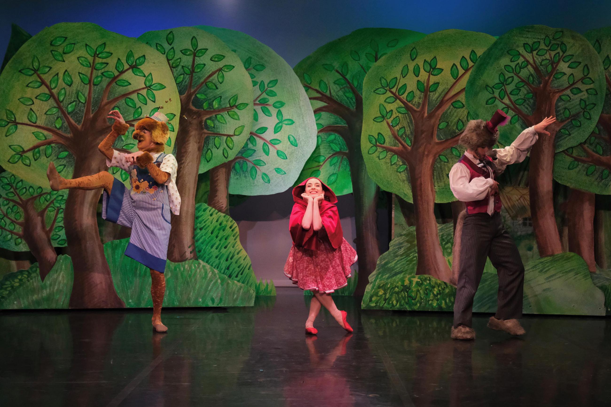 Three dancers on stage dancing in front of a woodland scene