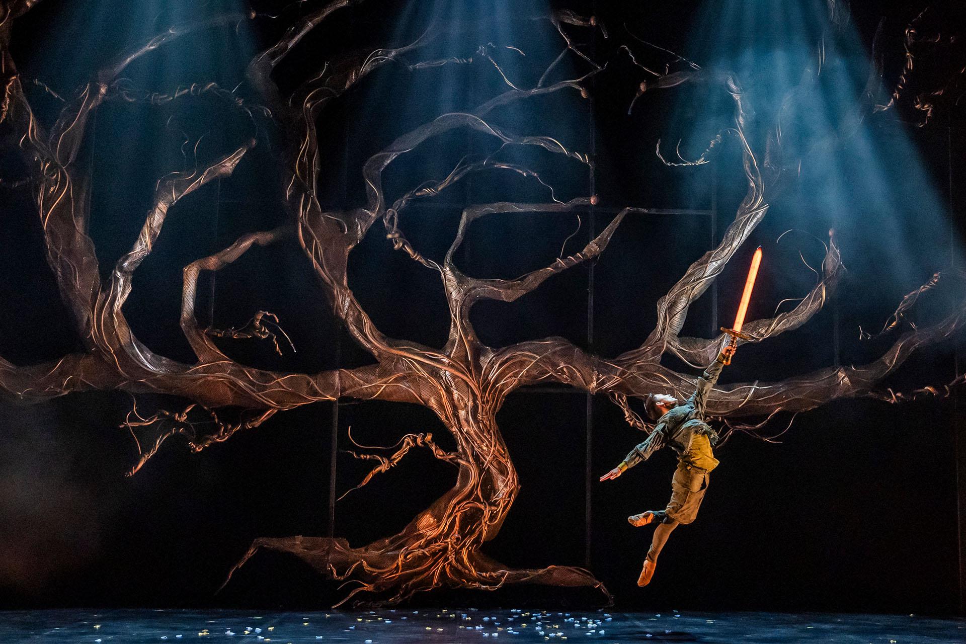 The tree of life, without leaves or magic, Merlin dances in front of it, a glowing sword raised high, inviting the magic into the kingdom