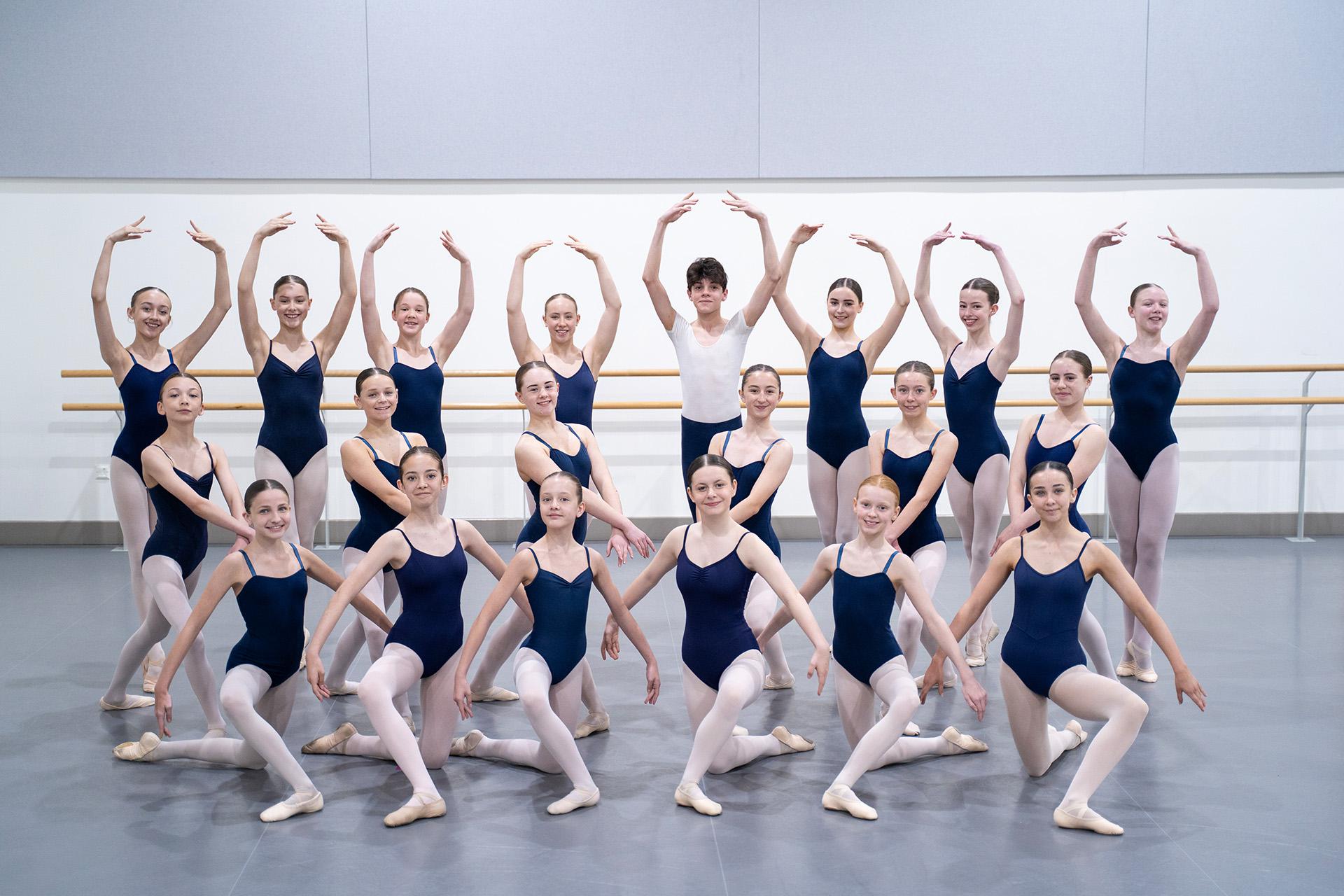 Class photo of 2025 Associates, women in blue leotards and white tights, man in white T-shirt and blue leggings