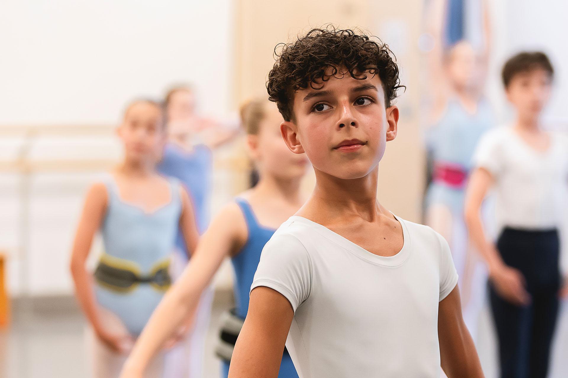 A young dancer with curly dark hair stands in a white t-shirt