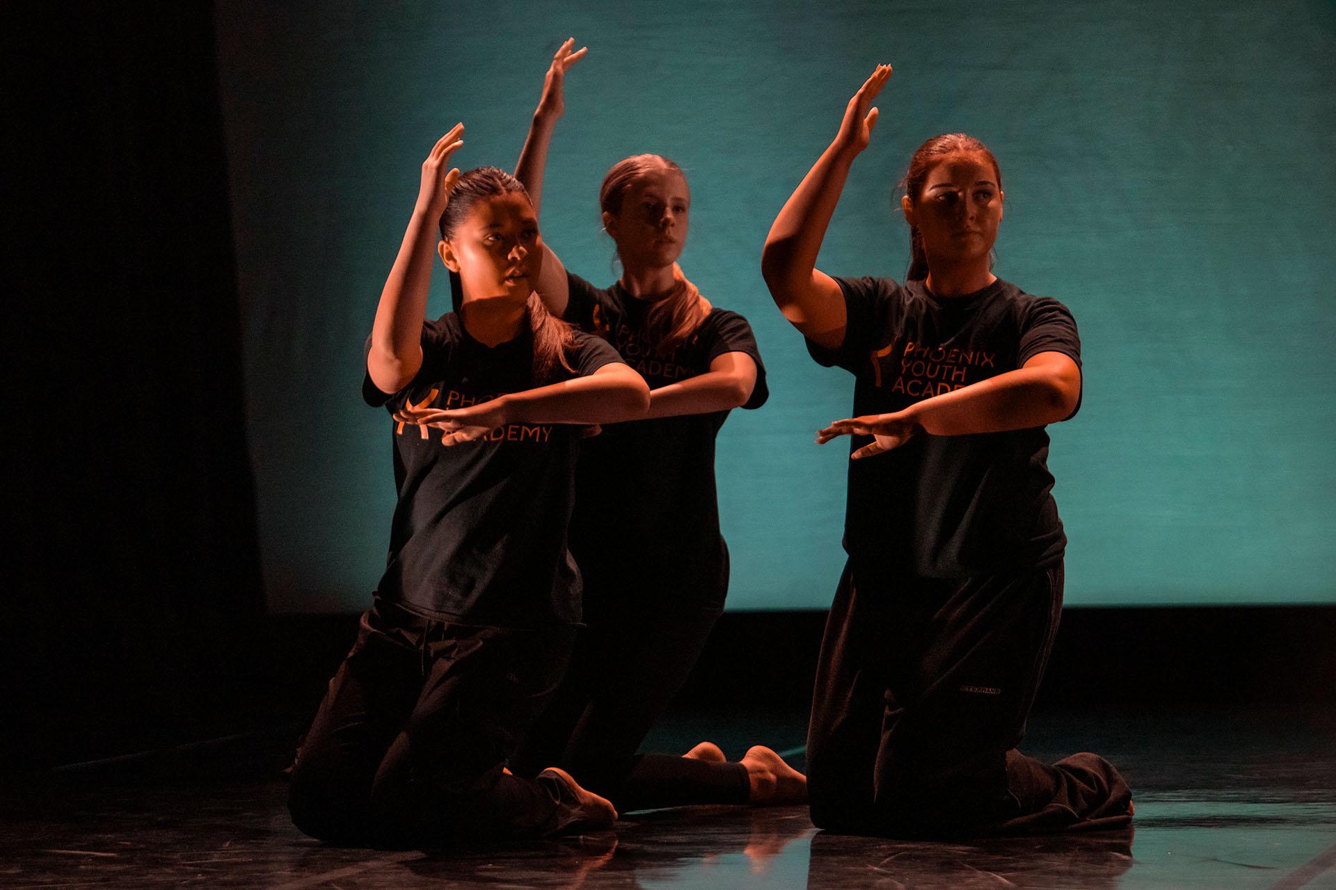 Three dancers left arm crossed in front of their bodies, right arm hinged at the elbow and forearm upright
