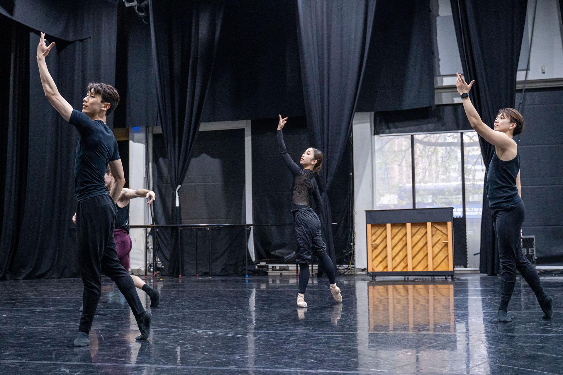 Three dancers in the rehearsal studio following the movements of the choreographer in front of them
