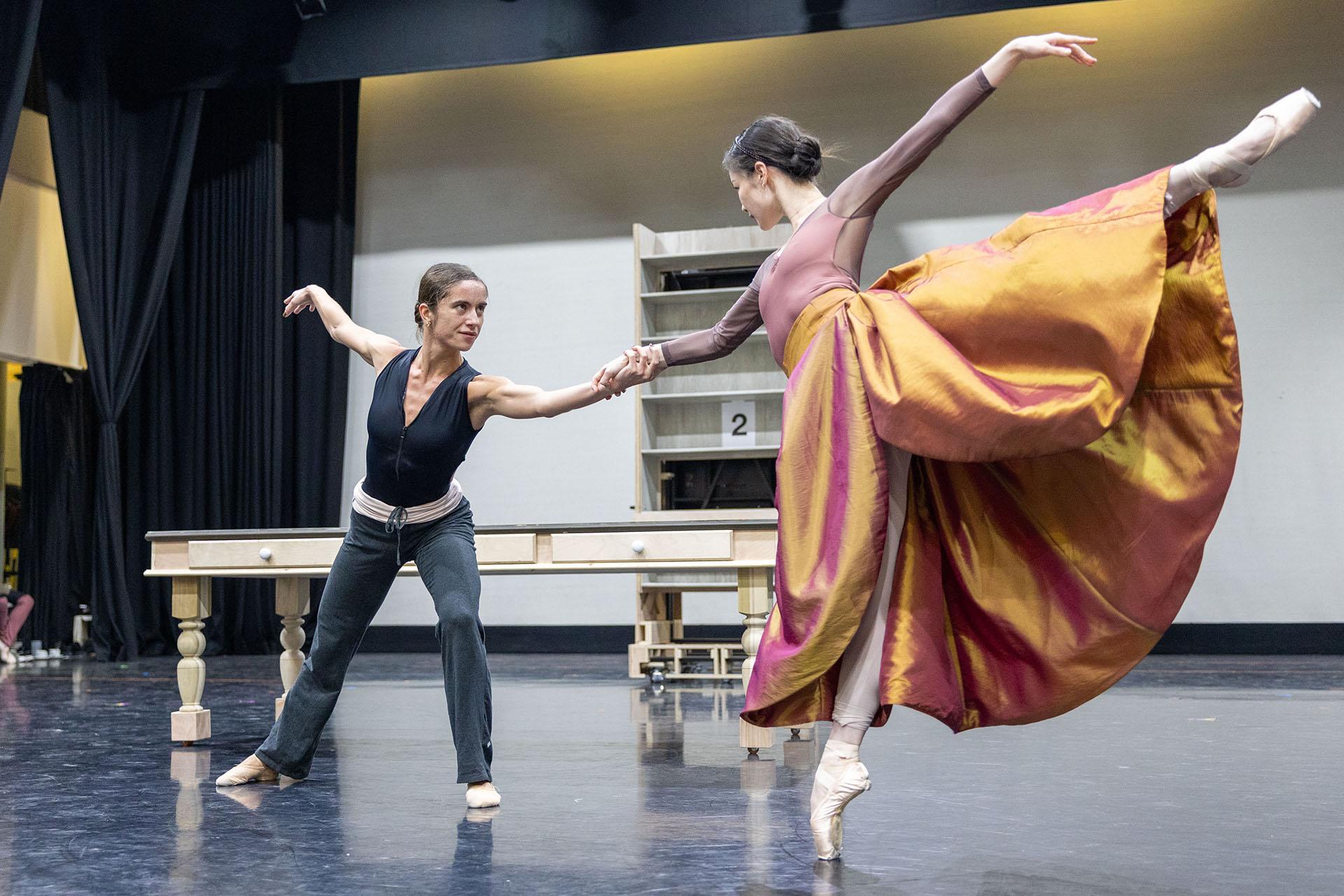 Two women rehearsing their roles in Gentleman Jack, one wearing dark, close-fitting clothes, the other in a voluminous, brightly colours skirt; they hold hands and look intently at each other