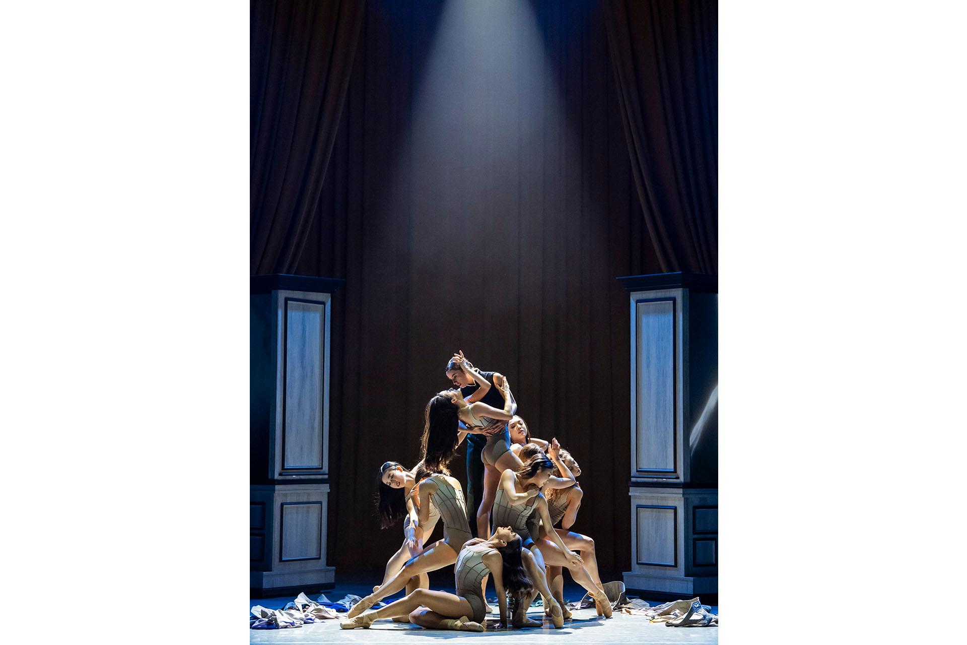 Bathed in light from above, Anne Lister holds her arm around her love surrounded by women who are wearing leotards