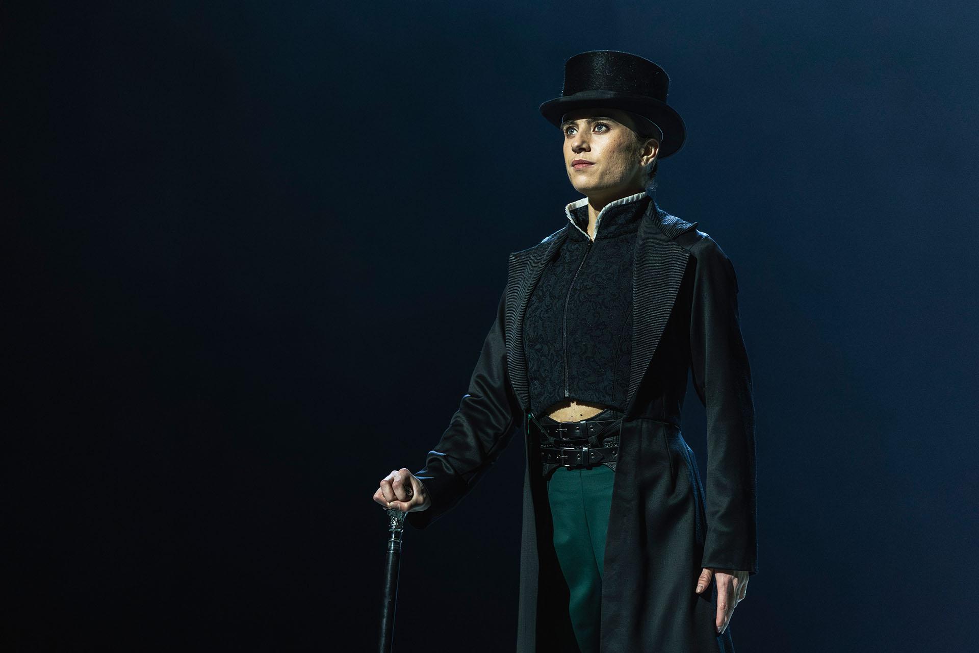 Standing proud, cane in one hand, hearing a tall hat and long coat, Anne Lister looks imperious
