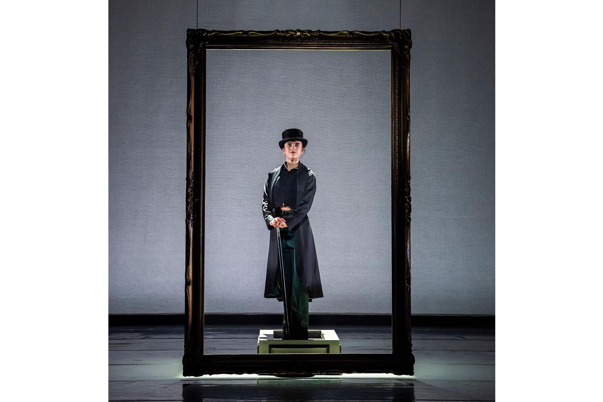 Literally in a picture frame, Anne Lister stands hands and feet together, wearing a long black coat, a hat and holding a cane.