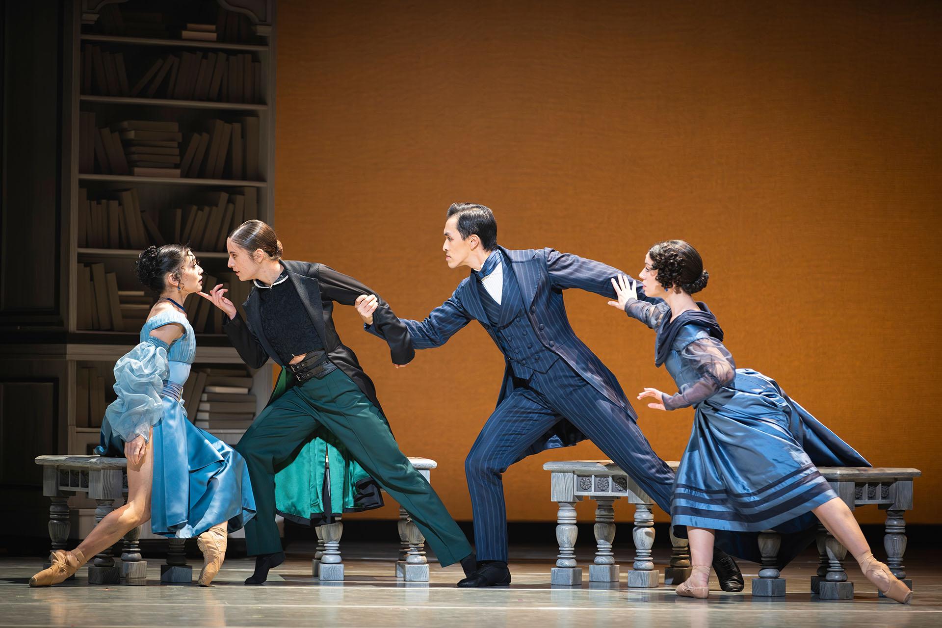 A woman in a blue dress looks lovingly at a woman holding her chin, she is held from behind by a man looking angry and be him is another woman looking concerned