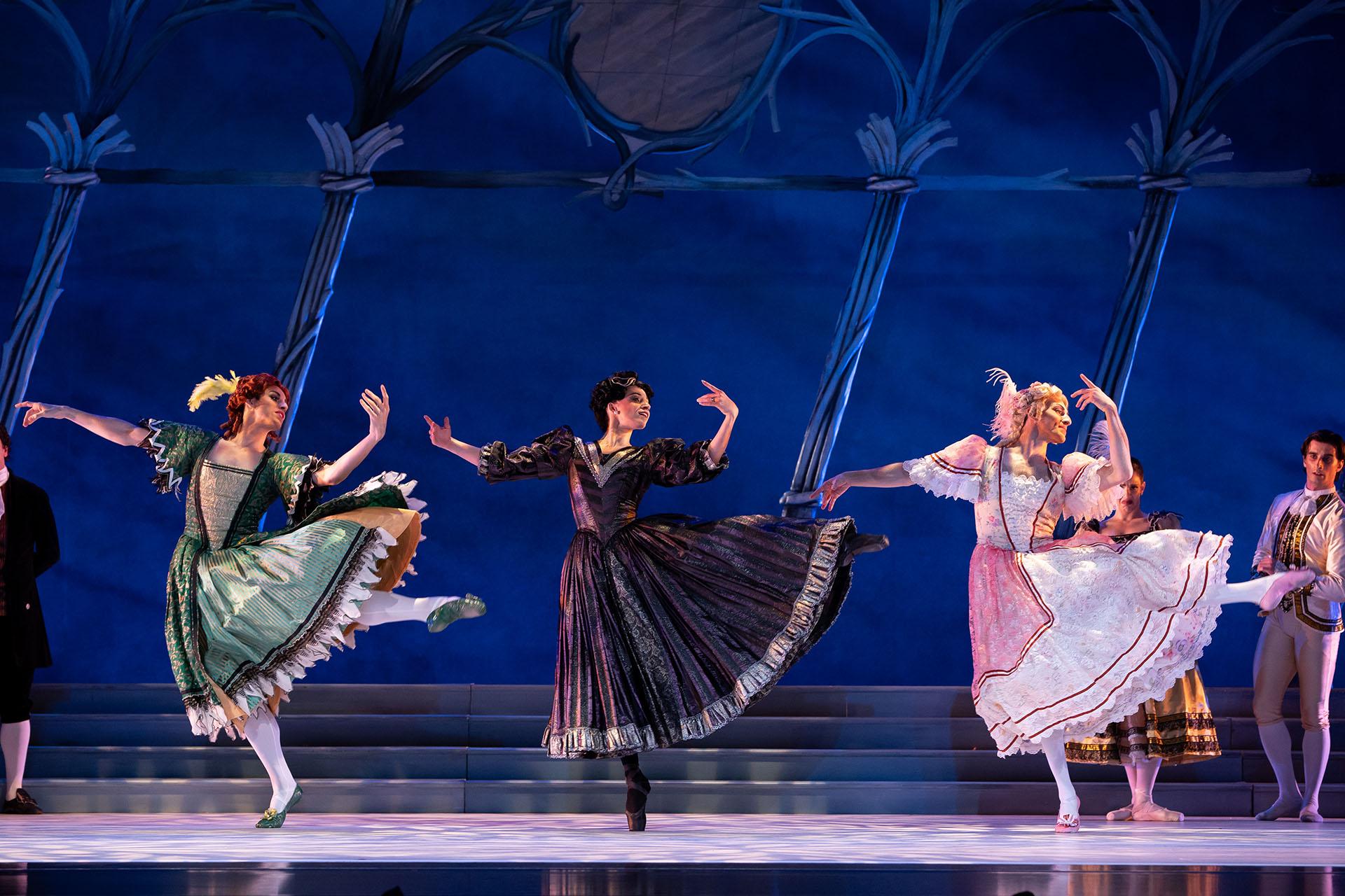 Three women, one in green, one in black, the other in pink, dance in unison