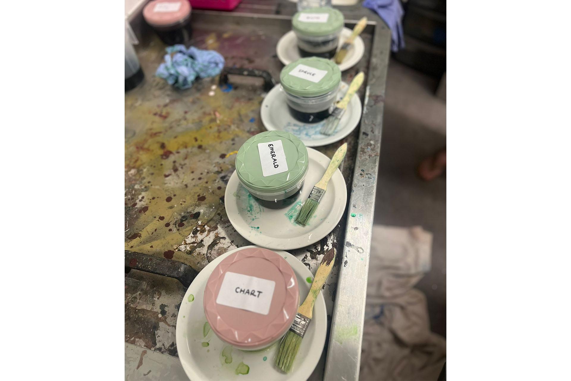 Four pots, one pink the others green on individual saucers with brushes to apply the dye they contain