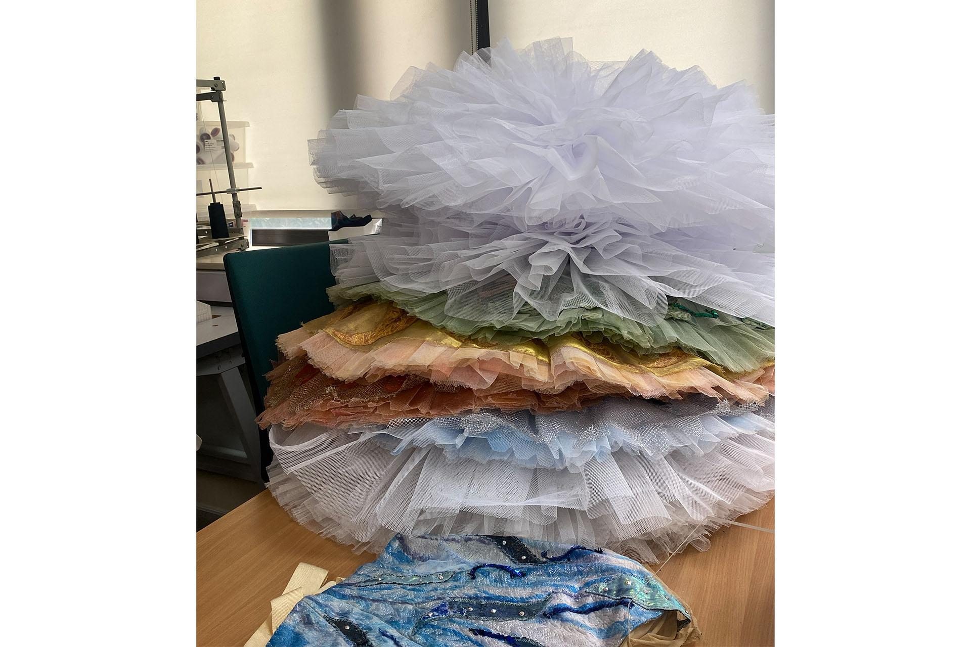 A vertical stack of tutus of different colours: white, green, cream, blue and umber