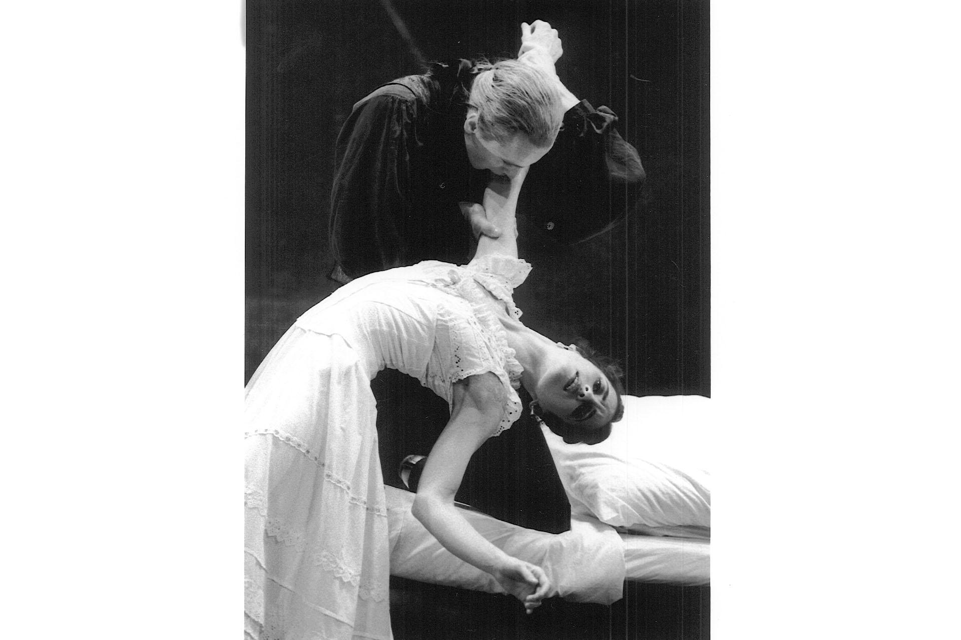 In black and white, a woman falls backwards as Dracula holds and bites her arm.