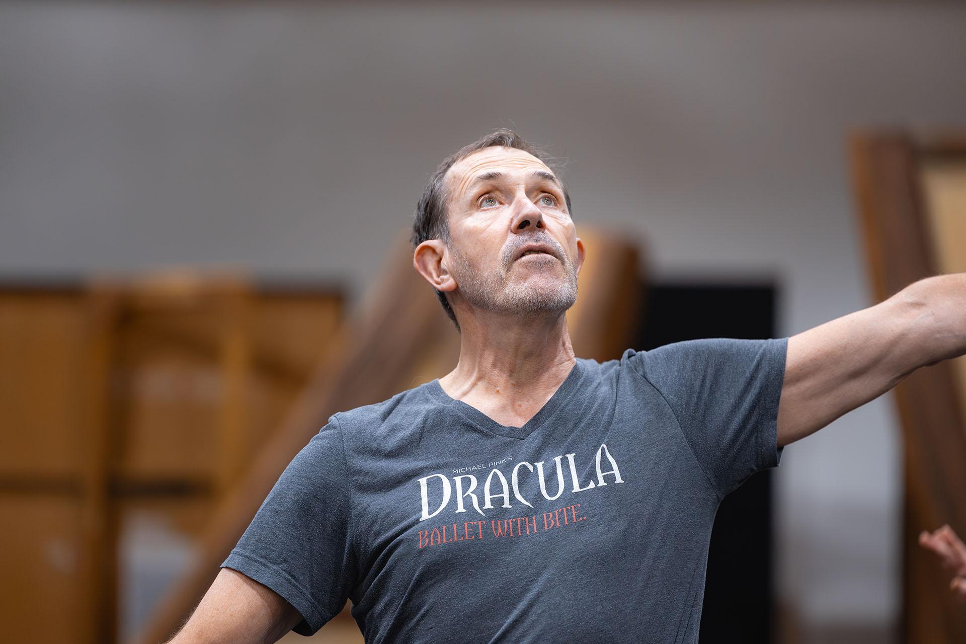 Choreographer, Michael Pink, wearing a grey T-shirt of his ballet Dracula with the log line, "Ballet With Bite", stands, head slightly raised