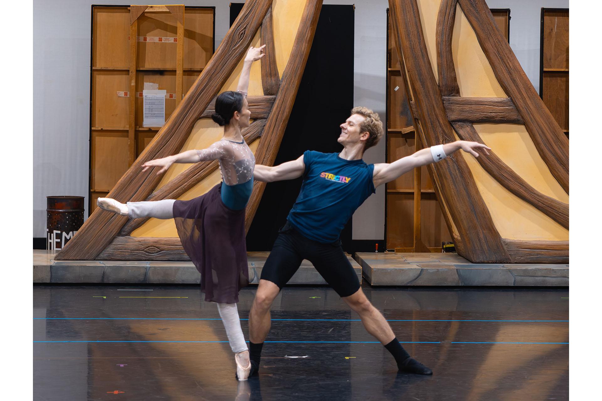 A dancer en pointe arabesque, the other steadying her balance with one hand holding her back and leaning back theatrically