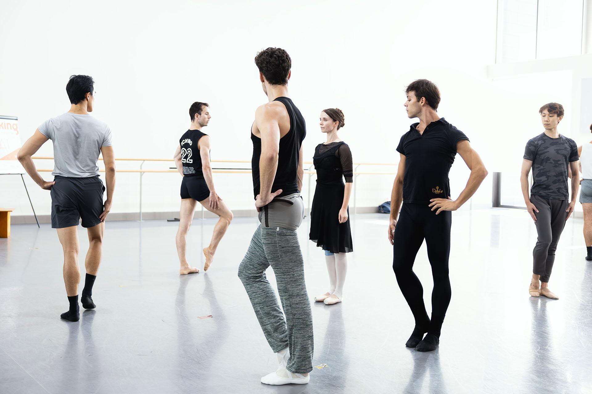 A dancer stands straight in a circle, other dancers form a circle around her, each looking in