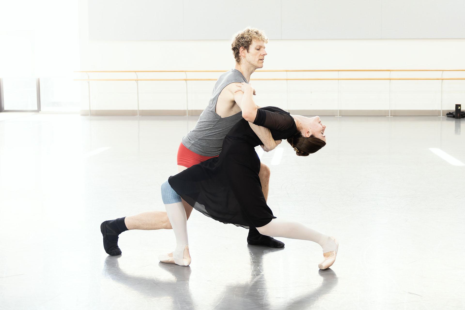 Two dancers low, knees bent, the woman dipped back, the man holding her behind her upper back so she doesn't fall