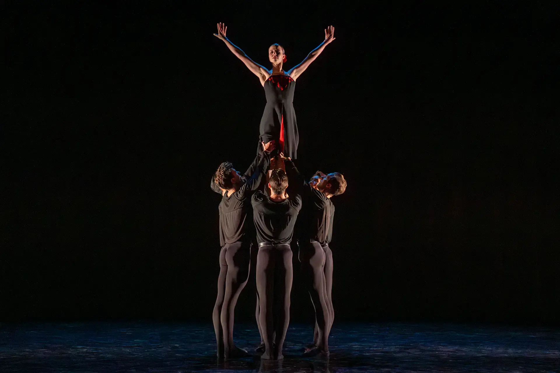 Three dancers support another, above their shoulders, her completely upright with her arms raised