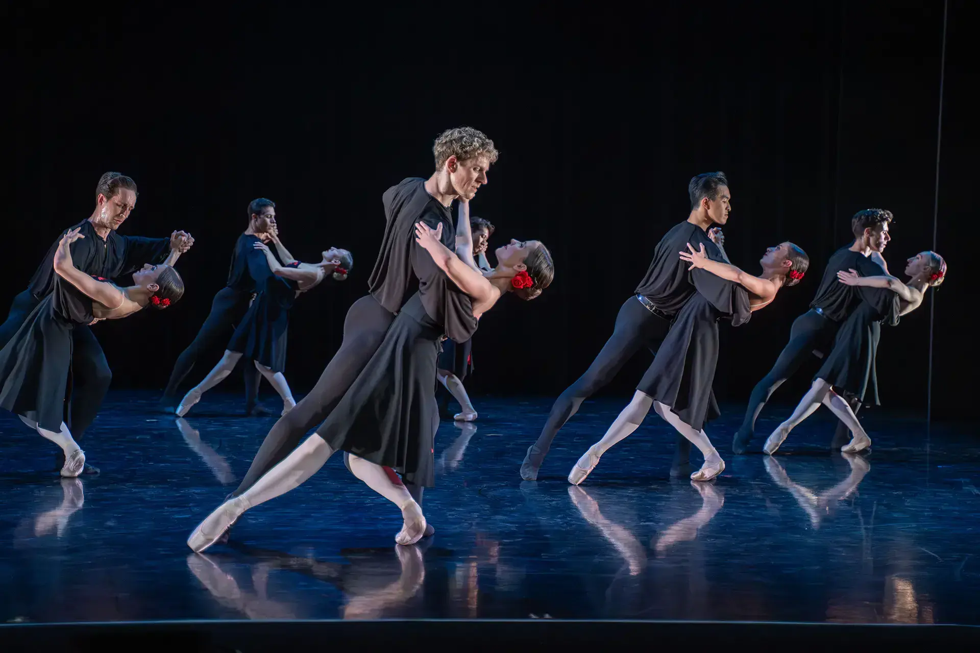 Six pair of dancers, each made up of a man and a woman, the woman leaning back and the man holding her by the waist