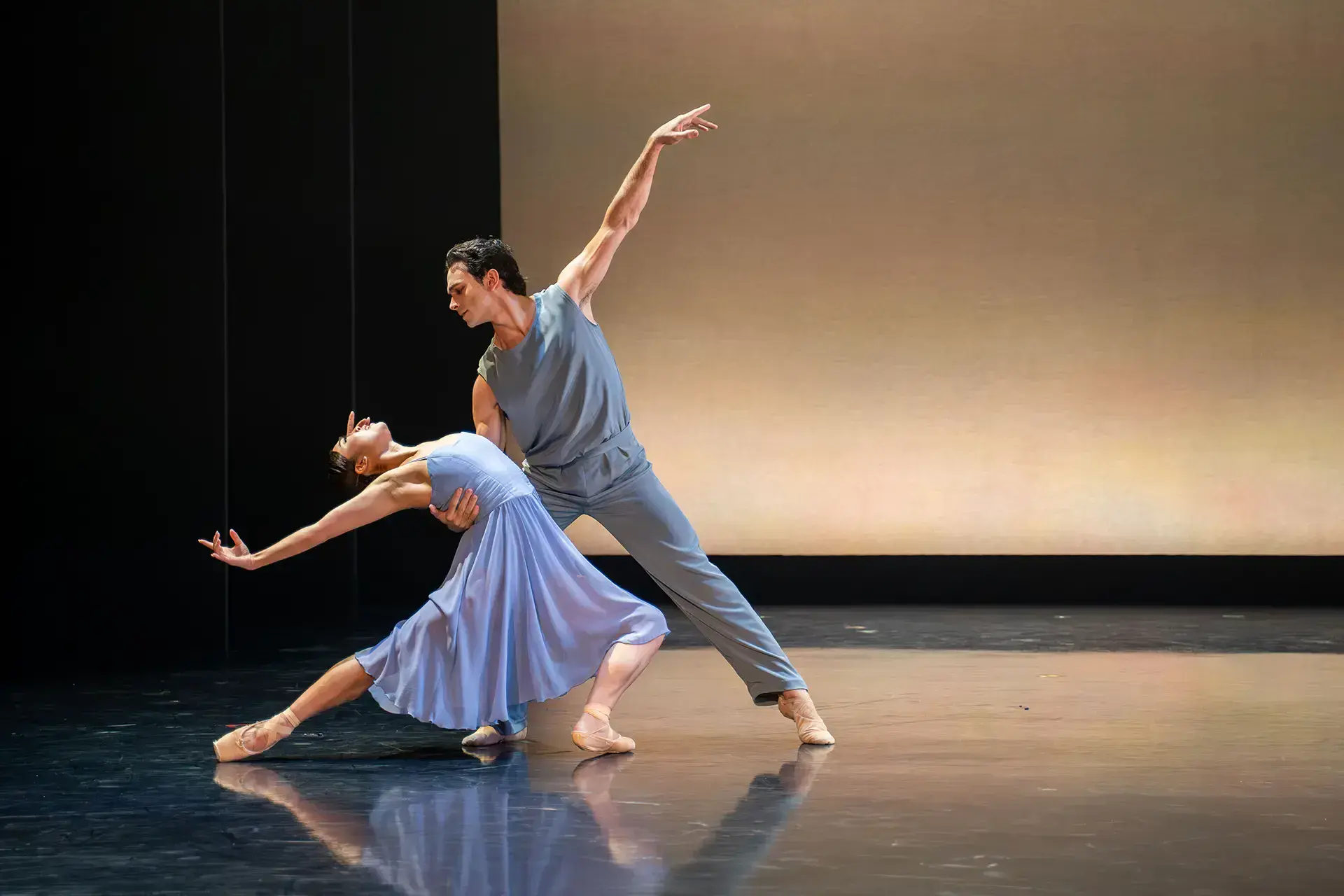 Dressed in shades of blue, a woman leans back, and a man holds her up with one arm behind her lower back