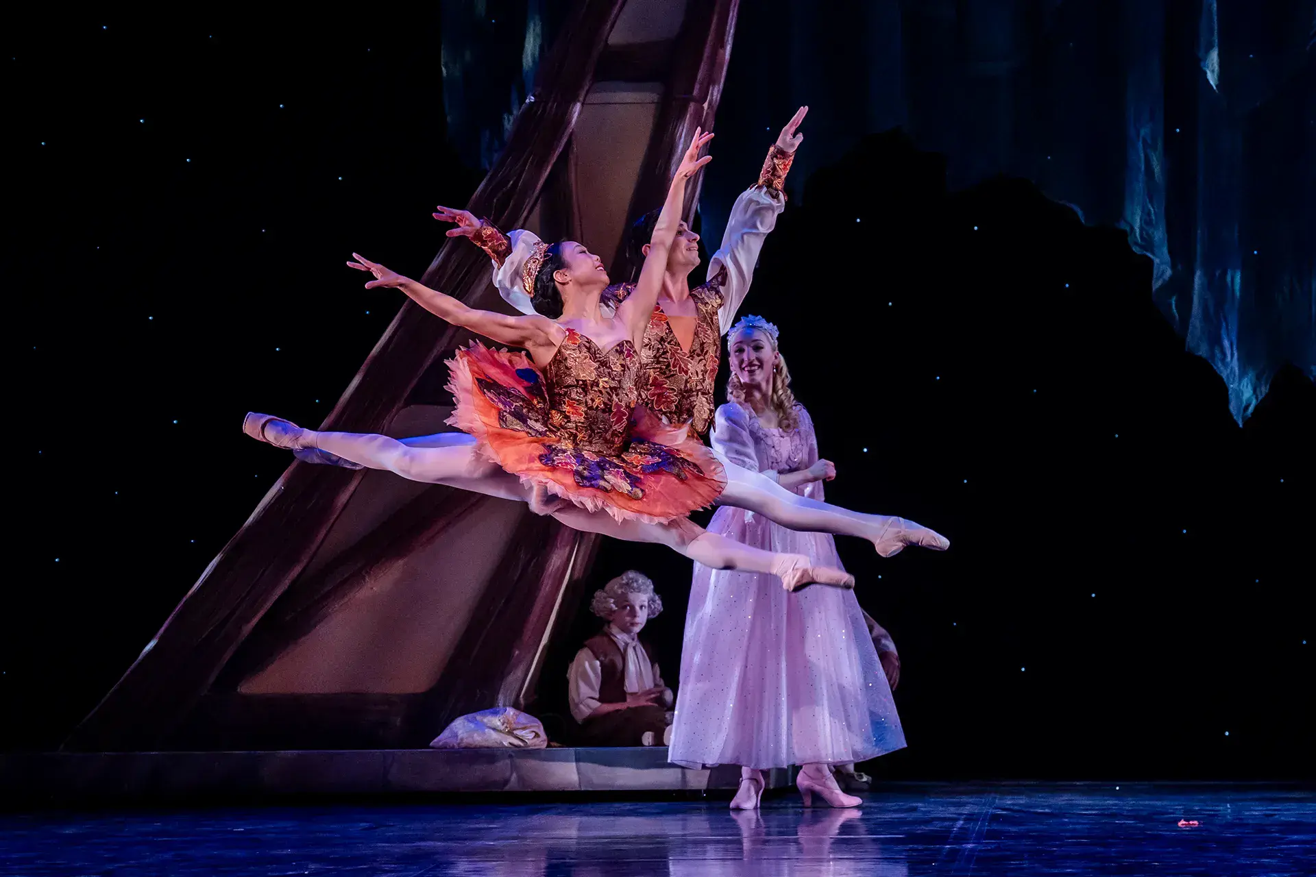 Leaping across the stage, dancers in their tutus, wearing poite shores and looking up