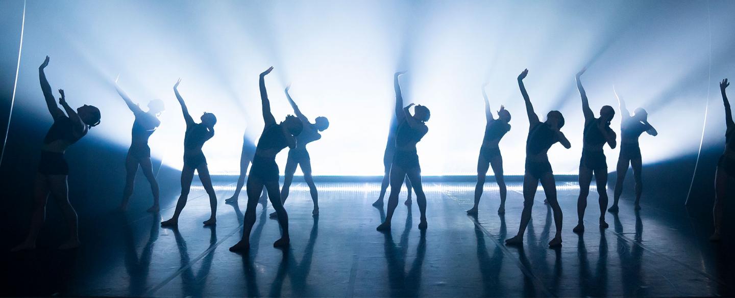 Northern Ballet dancers perform in unison through a flood of light. Photo Emma Kauldhar.
