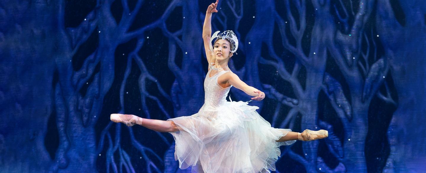 Ayami Miyata in a sparkline whide snowflake dress leaps in a grand jeté