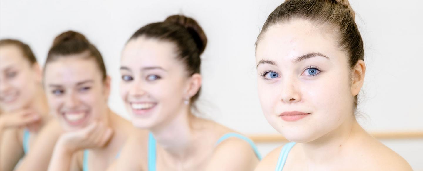 1 dancer looks into the camera as three dancers look on smiling