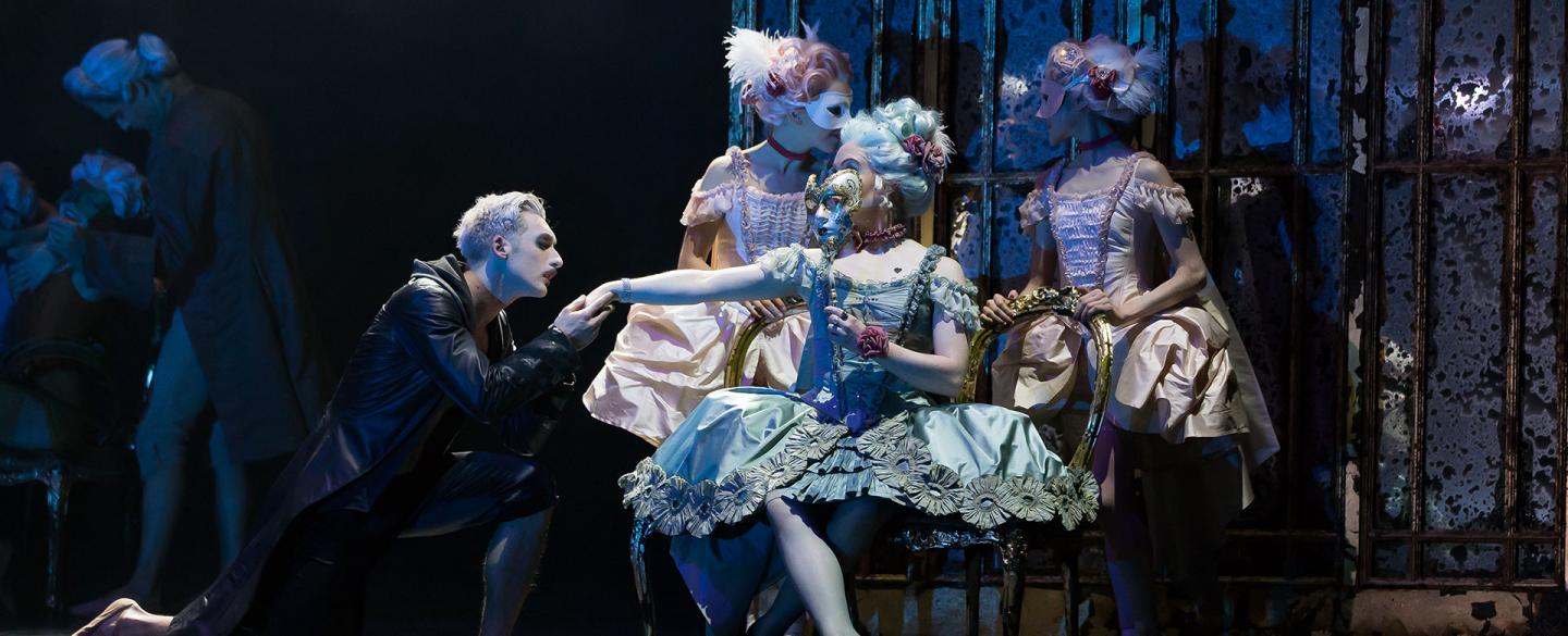 Casanova goes down on one knee as his kisses the back of masked Madame de Pompadour's hand