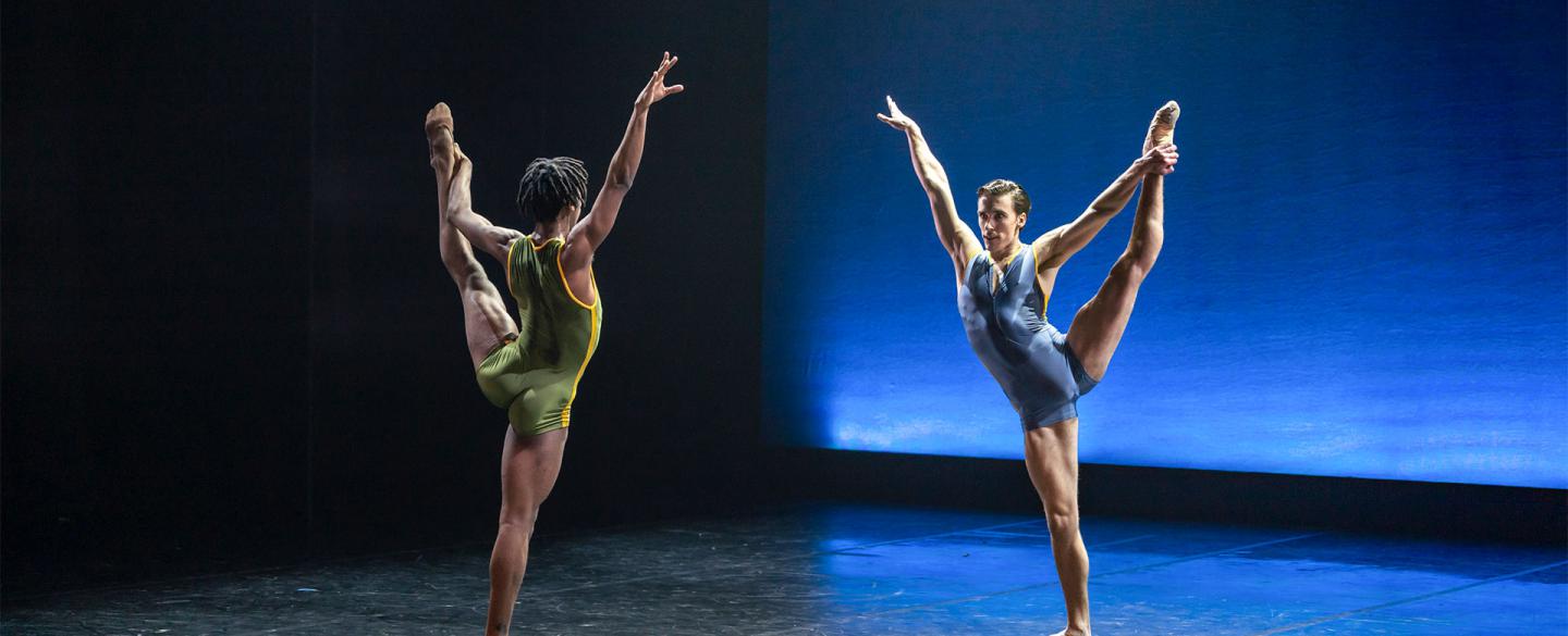 Mlindi Kulashe and Andrew Tomlinson face each other as they reach high with one arm whole holding their left leg aloft with the other