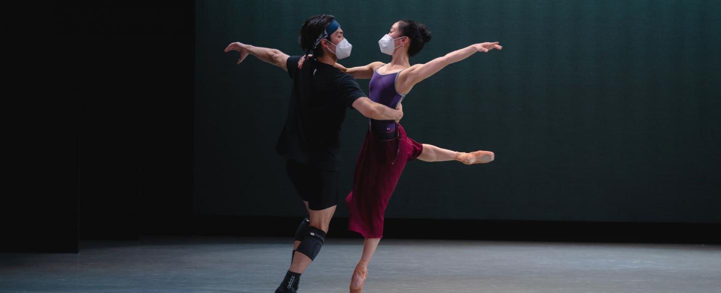 A female dancer stands en pointe as her partner supports her at the waist, they appear to mid-spin