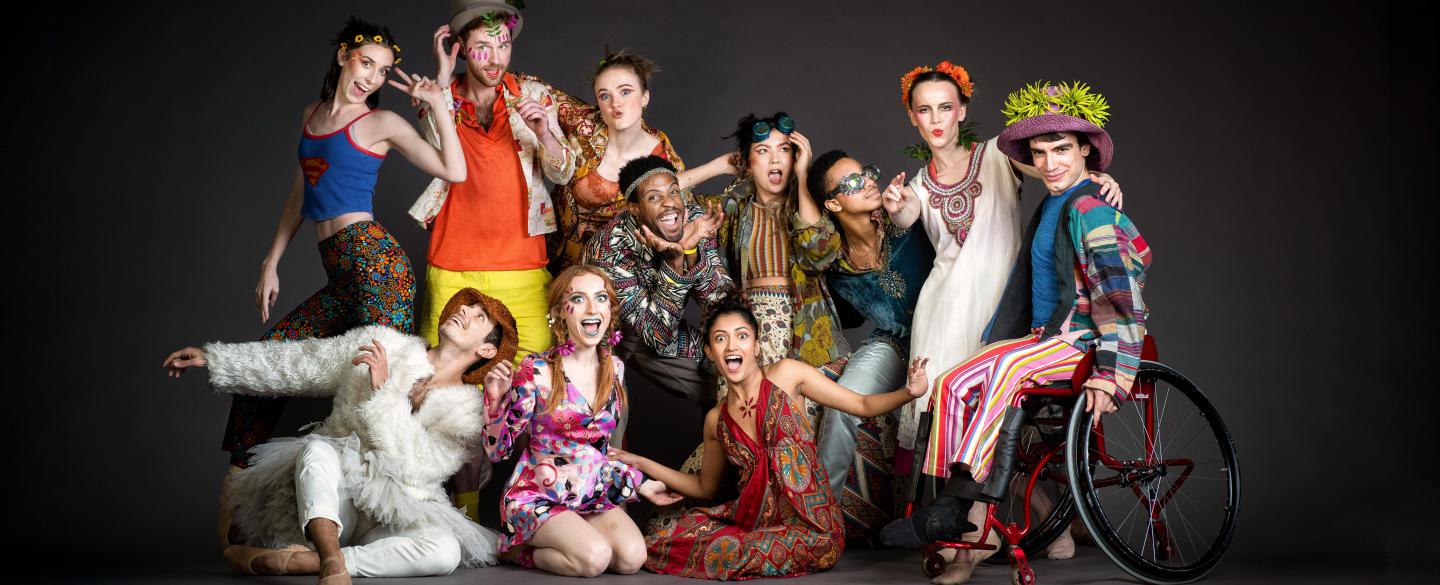 A group of 11 dancers pose towards the camera in brightly coloured clothes.