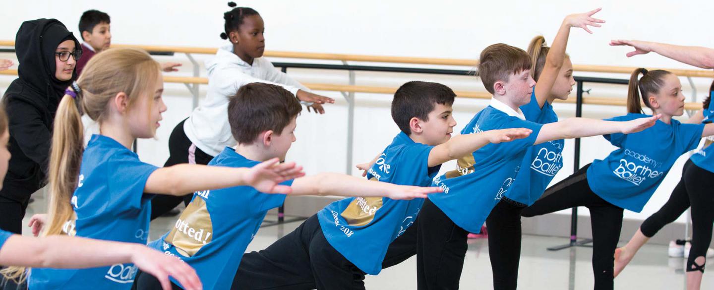 Group of you people practicing balancing on one leg with one leg stretched behind them and balanced from their bodies leaning forward.