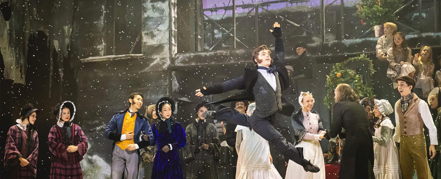Bob Cratchit leaps into the air as snow falls and townspeople watch on in delight