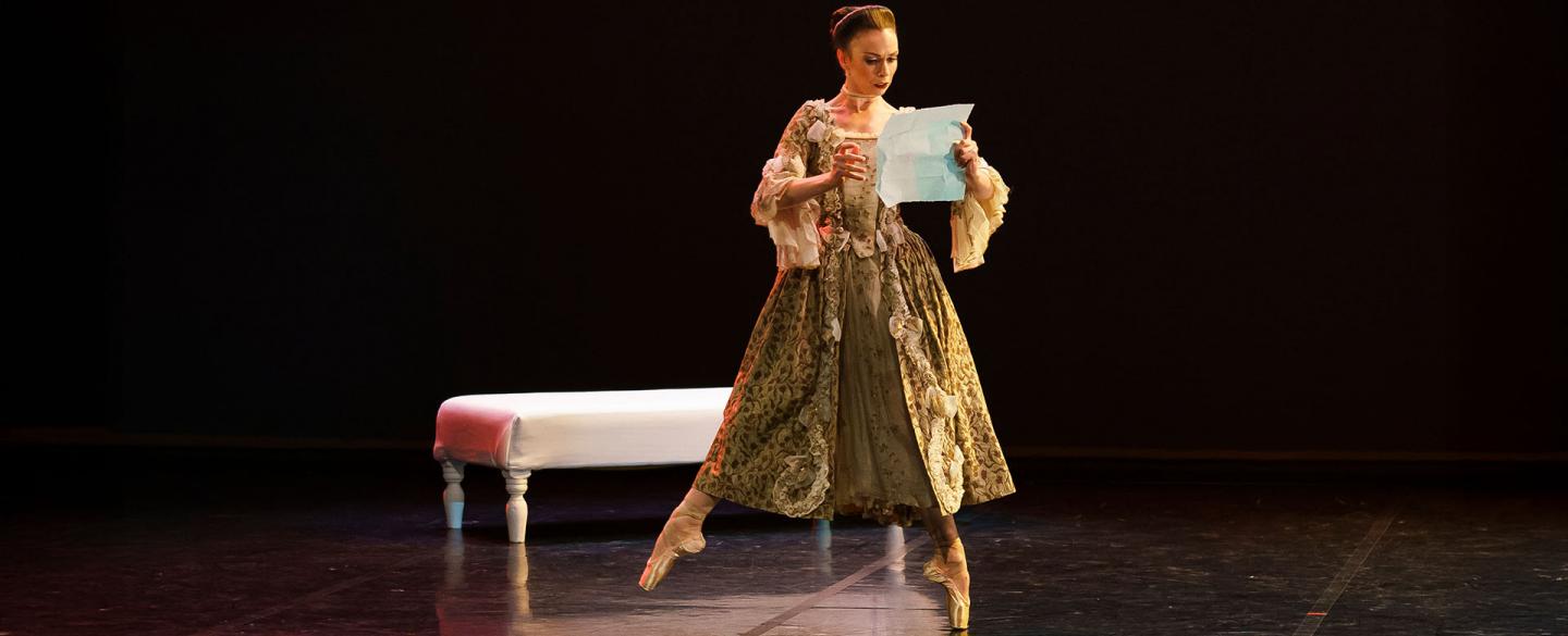 Dancer in French Regency attire and on pointed feet reads a letter