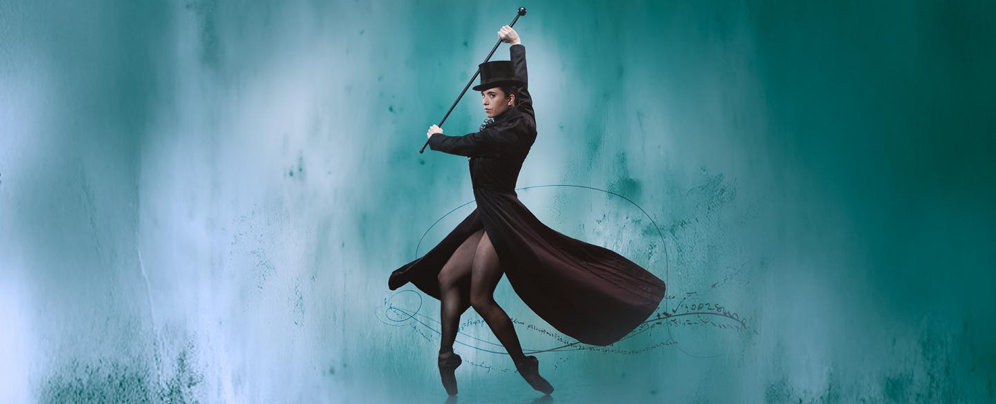 Woman holding riding crop, standing on black pointe shoes wearing a long black coat and hat
