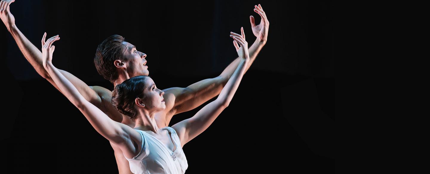Two dancers in white looking into the distance, hands raised