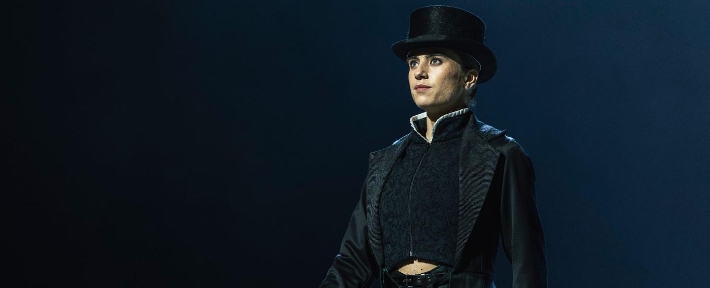 Standing proud, cane in one hand, hearing a tall hat and long coat, Anne Lister looks imperious