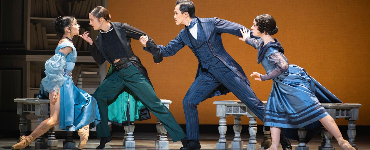 A woman in a blue dress looks lovingly at a woman holding her chin, she is held from behind by a man looking angry and be him is another woman looking concerned