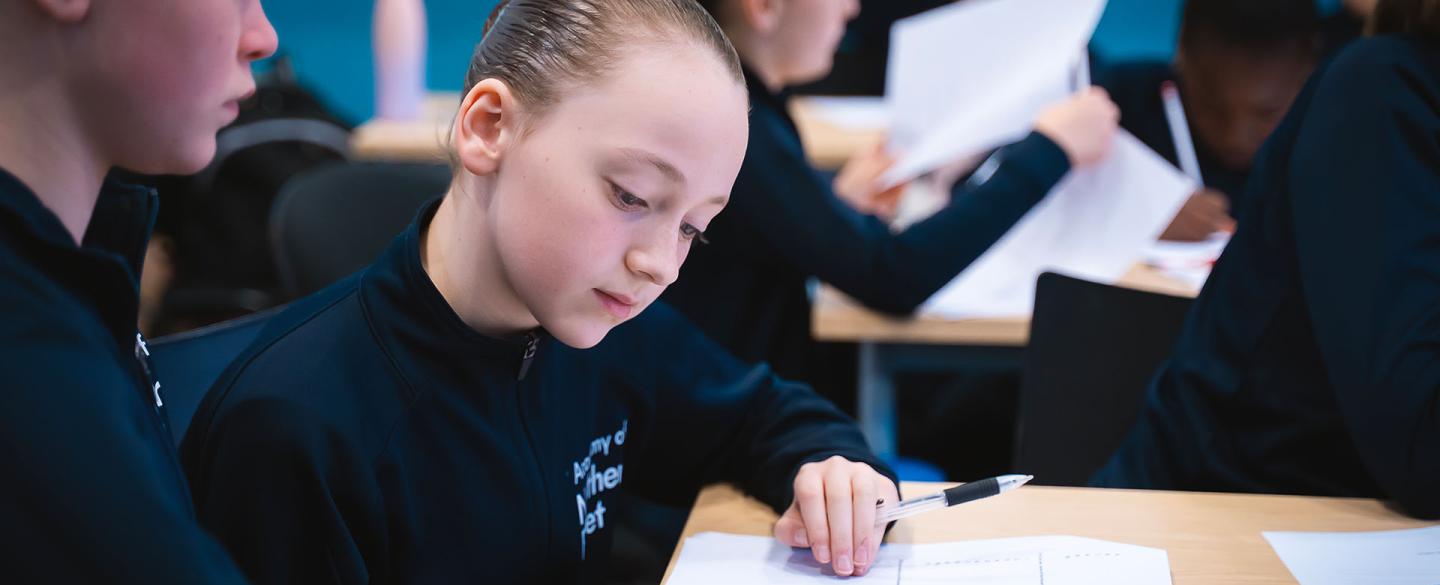 Students in dark tracksuits in a class looking at a worksheet