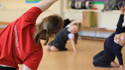 Teacher leads a class in reaching over their heads