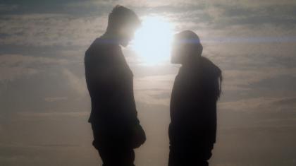 Two people stare at each other as the sun sets behind them