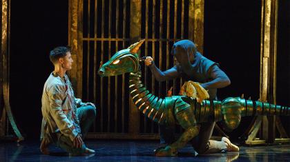 Two dancers on stage, one is holding a dragon puppet.