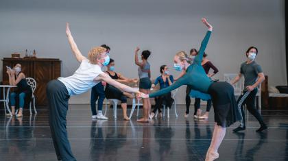 Holding hands, two dancers at arms length bow to each other while stretching an arm behind them