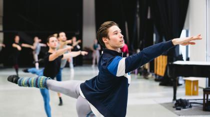 A Northern Ballet dancer, facing the right with their right arm stretched out and their left leg stretched behind them.