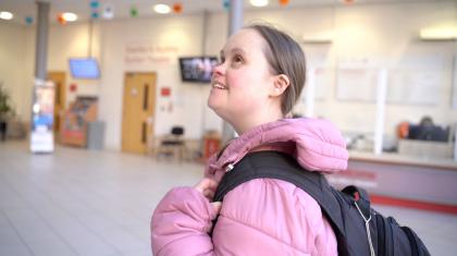 A girl in a pink jacket and black backpack in Northern Ballet's building foyer.