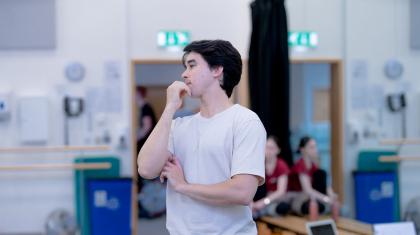 A looks thoughtfully at something in the distance whilst standing in a dance studio. 