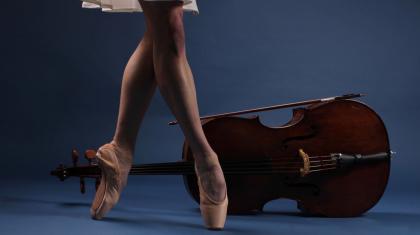 Photo of the bare lower legs wearing pointe shoes in front of a viola places on its side all against a blue background