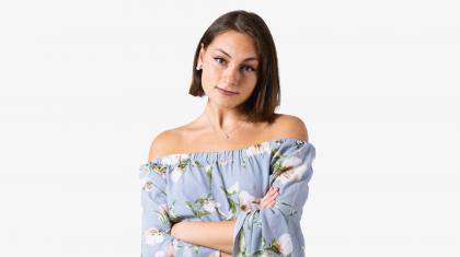 A headshot of a woman looking forward with dark brown hair and a light blue flowery top
